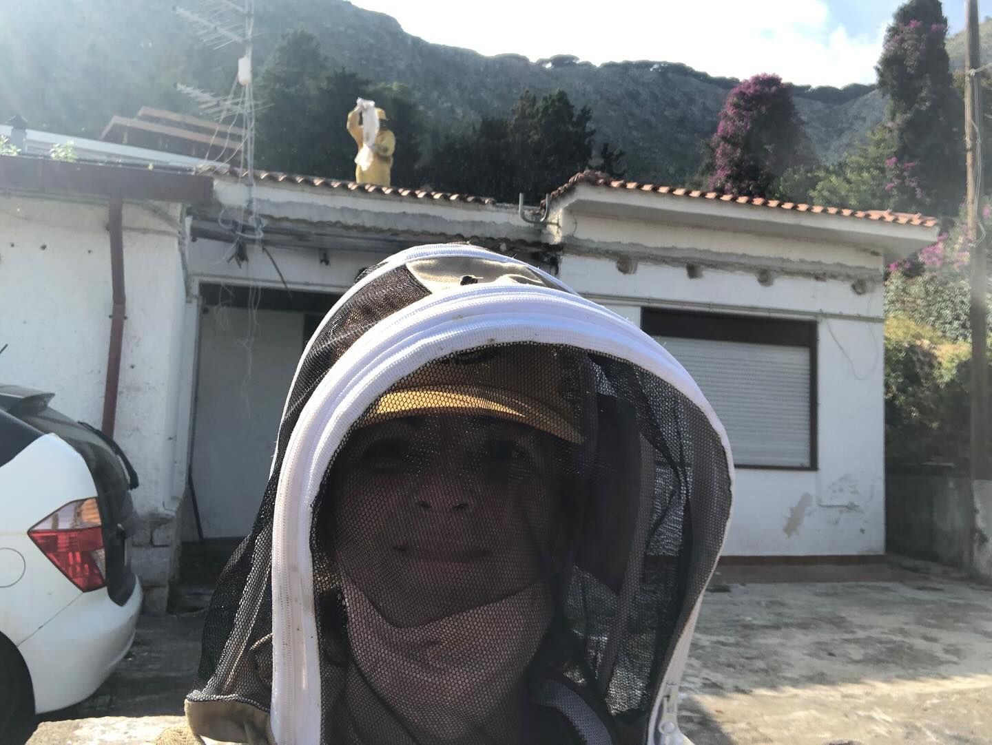 Autoritratto con la maschera da apicoltore prima di un intervento, davanti a una casa